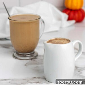 Mug of coffee with pumpkin spice creamer in it next to a small pitcher with additional creamer.