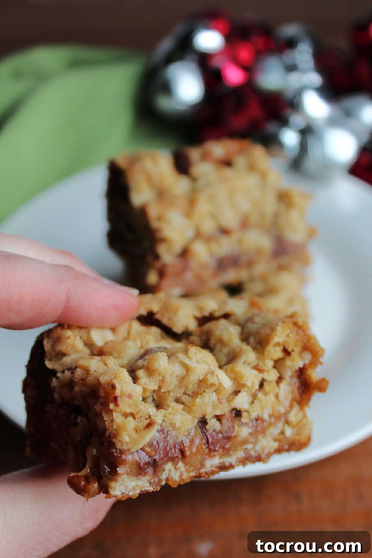 A hand holding an oatmeal caramelita bar, showcasing its golden crust and the tempting, gooey caramel, chocolate, and pecan filling.