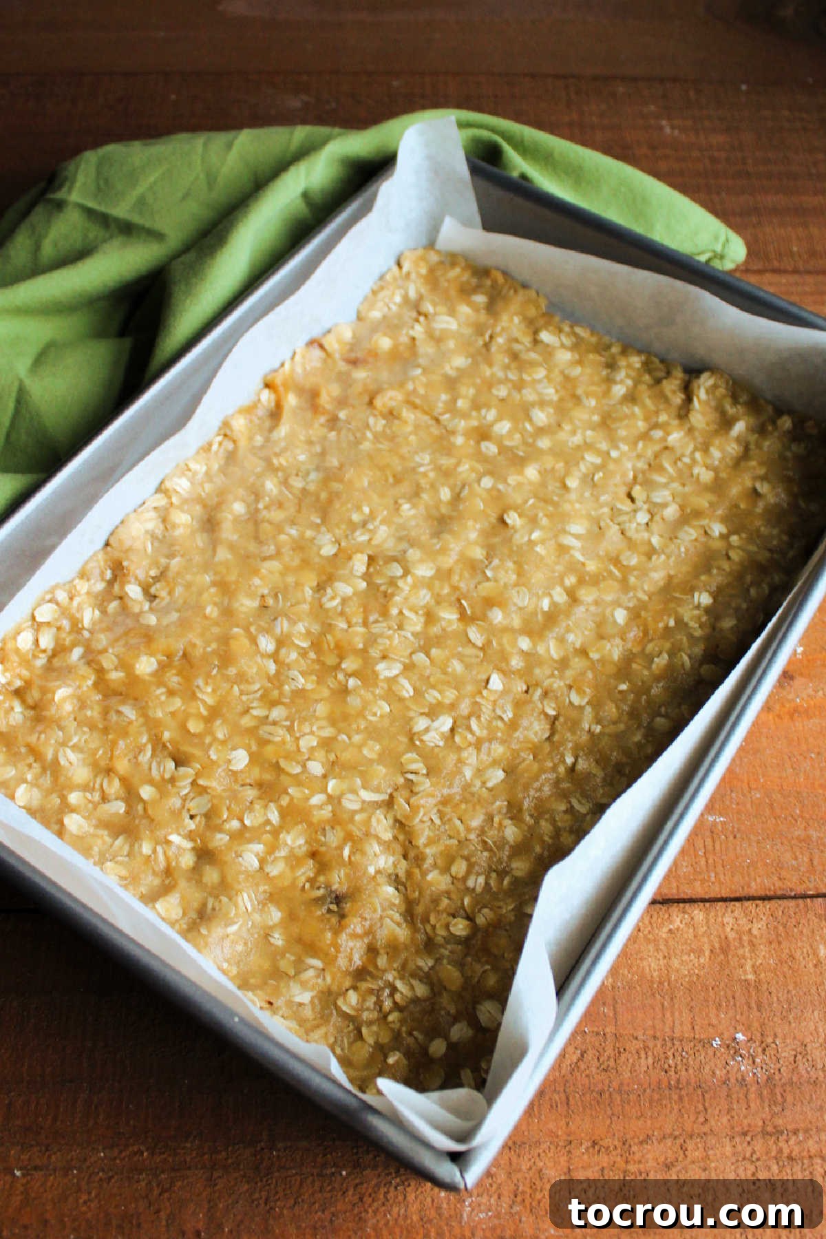 Half of the oatmeal cookie dough pressed evenly into the bottom of a 9x13 inch baking pan, forming the base for the caramelitas.