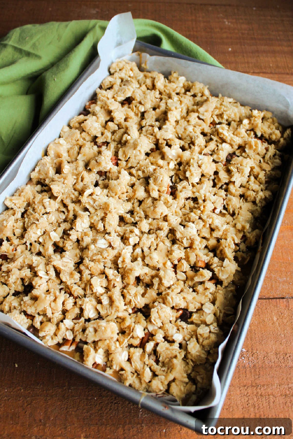 Small, crumbly bits of the remaining oatmeal cookie dough sprinkled evenly over the caramel, chocolate chip, and pecan layer, ready for the final bake.