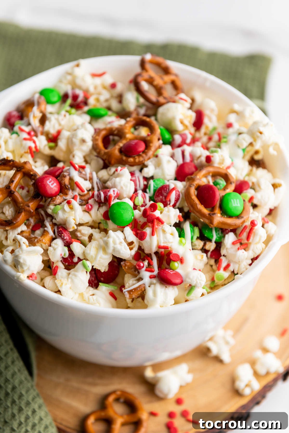 A large, inviting white serving bowl generously filled with a vibrant sweet and salty Christmas crunch snack mix, showcasing fluffy popcorn, crisp pretzels, colorful M&Ms, and delicate white chocolate drizzles. Perfect for sharing at holiday gatherings.