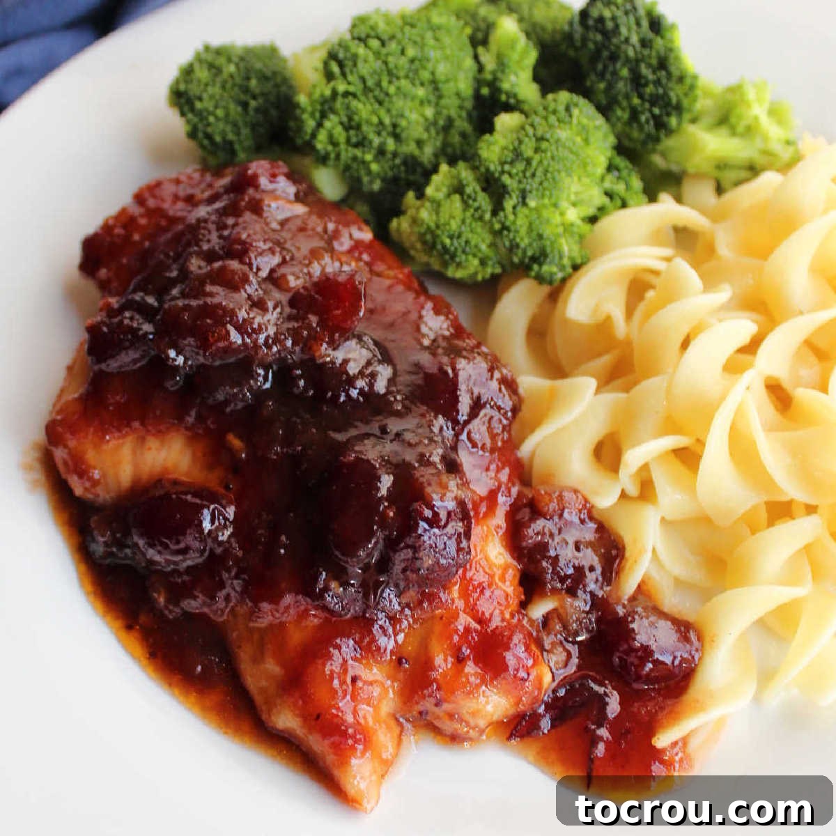 Close up of chicken breast topped with sauce made with whole cranberries and catalina dressing served with pasta and broccoli.