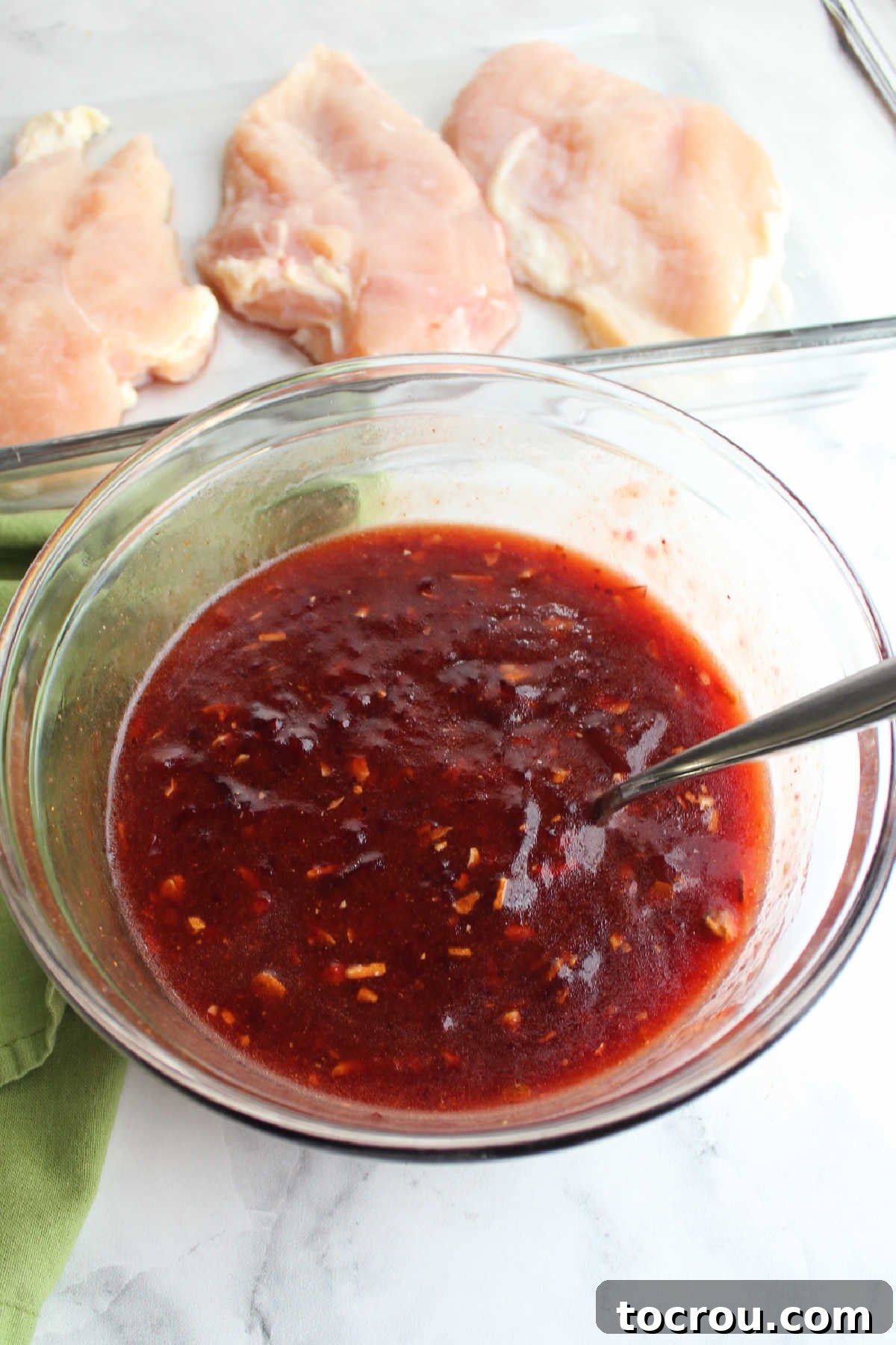 Bowl of sauce made from dressing, onion soup mix and cranberry sauce with pan of chicken breasts in the background.