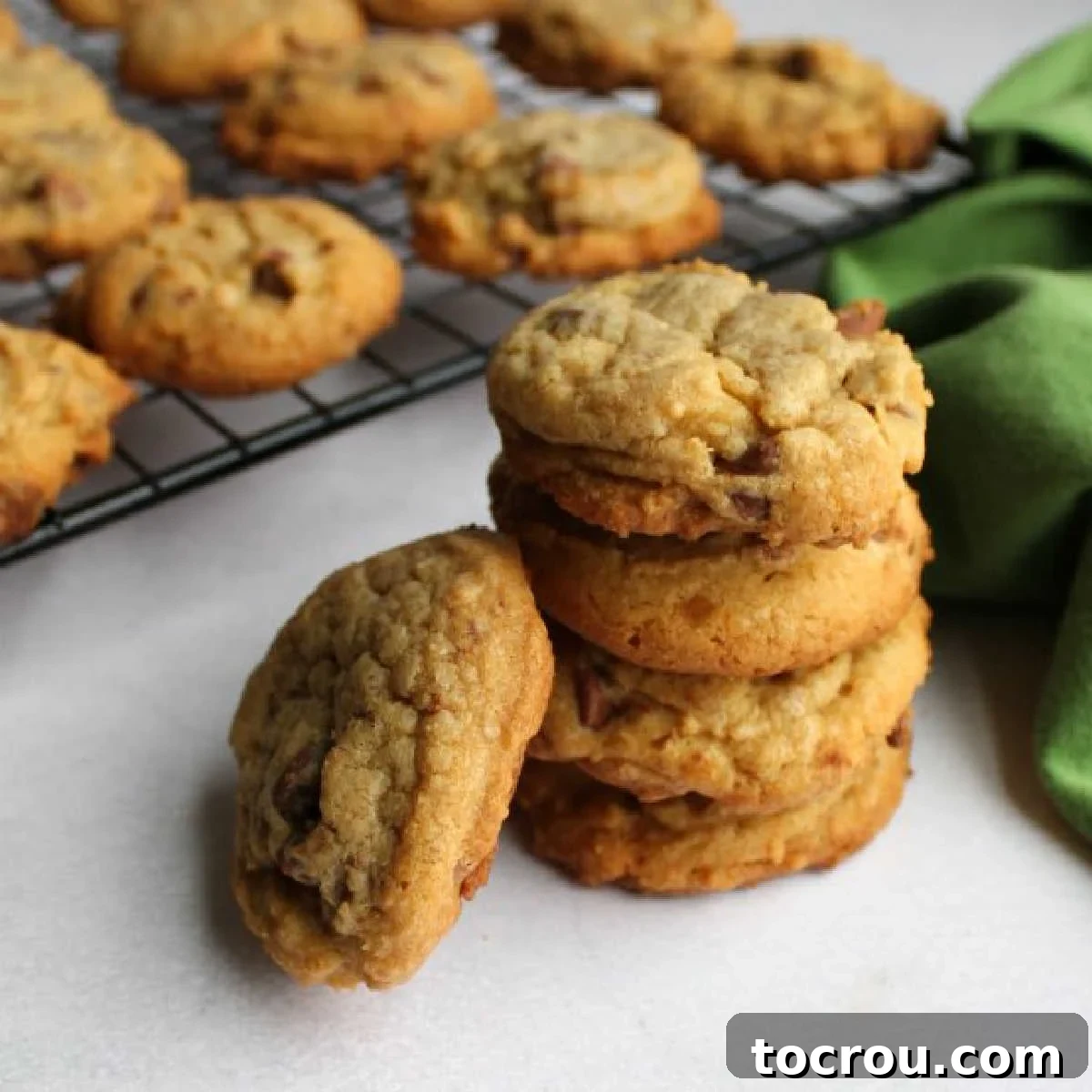 stack of soft chocolate chip cookies with vanilla pudding, with more on cooling rack in the background.