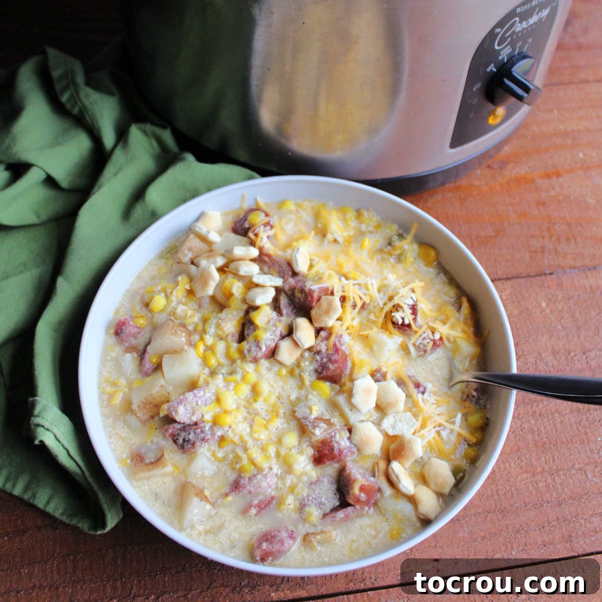 Bowl of creamy kielbasa, corn and potato chowder next to slow cooker.