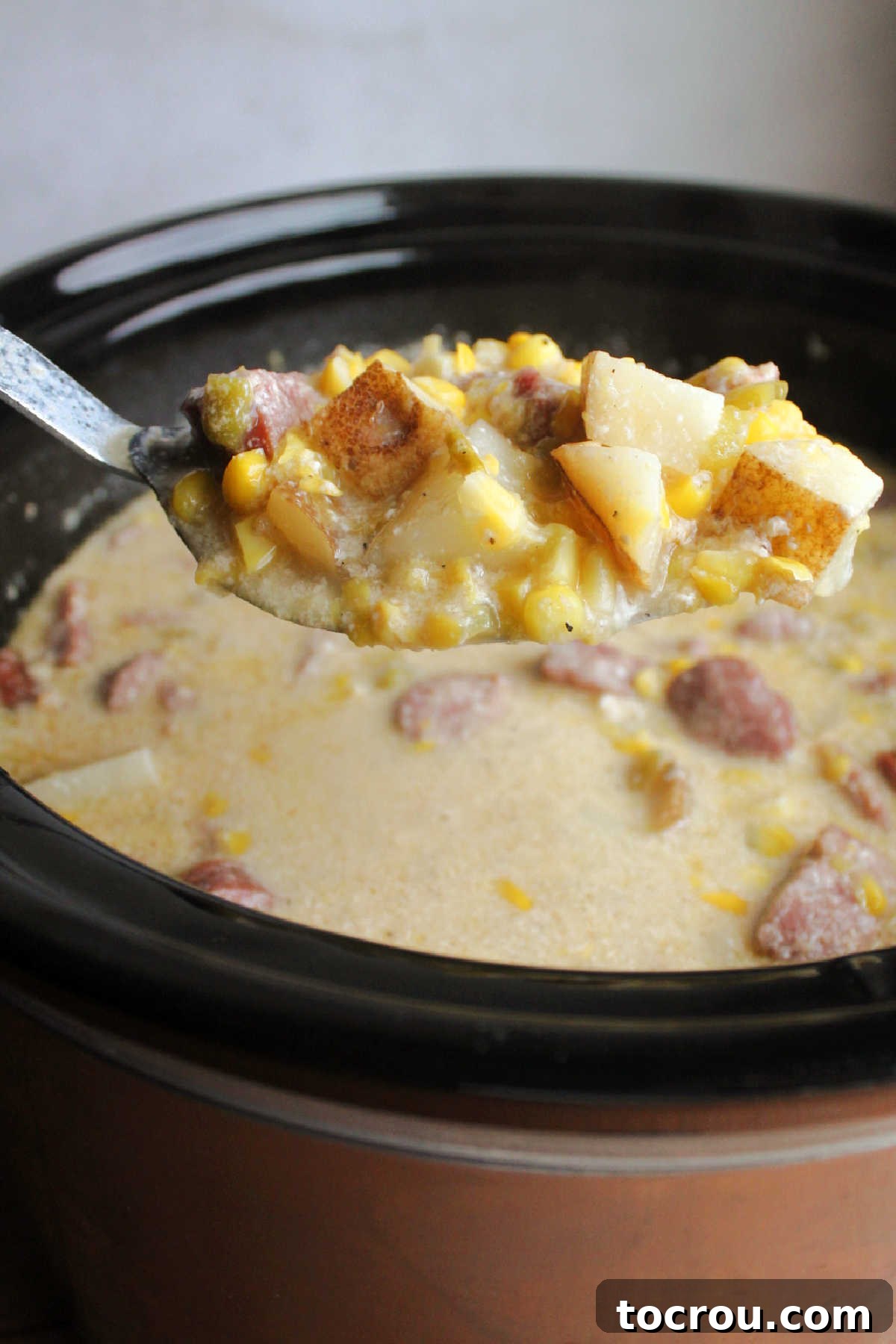 Serving spoon filled with helping of chowder, ready to be served. 