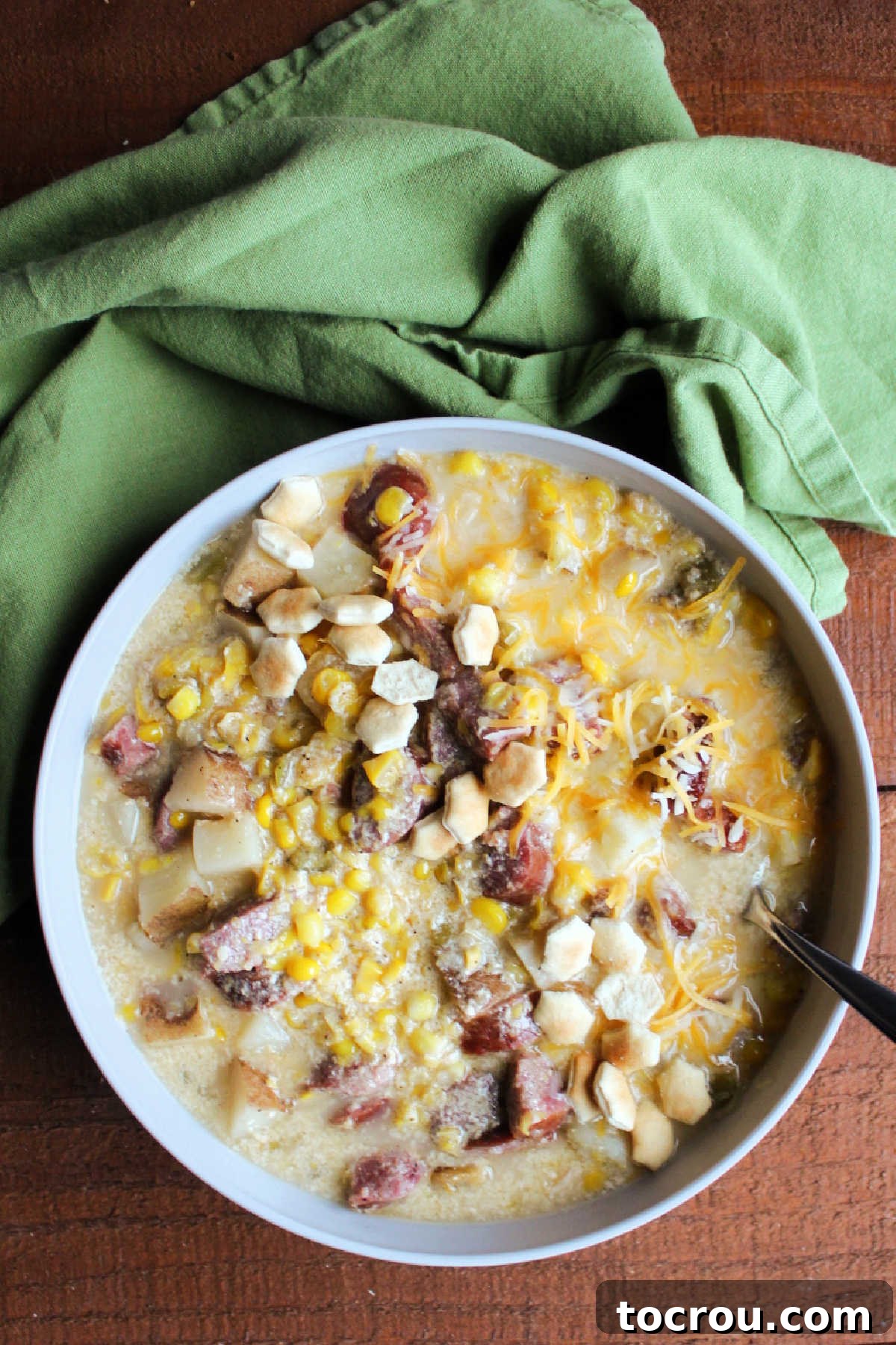 Bowl of kielbasa chowder served with shredded cheese and oyster crackers.