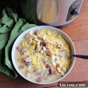Bowl of creamy kielbasa, corn and potato chowder next to slow cooker.