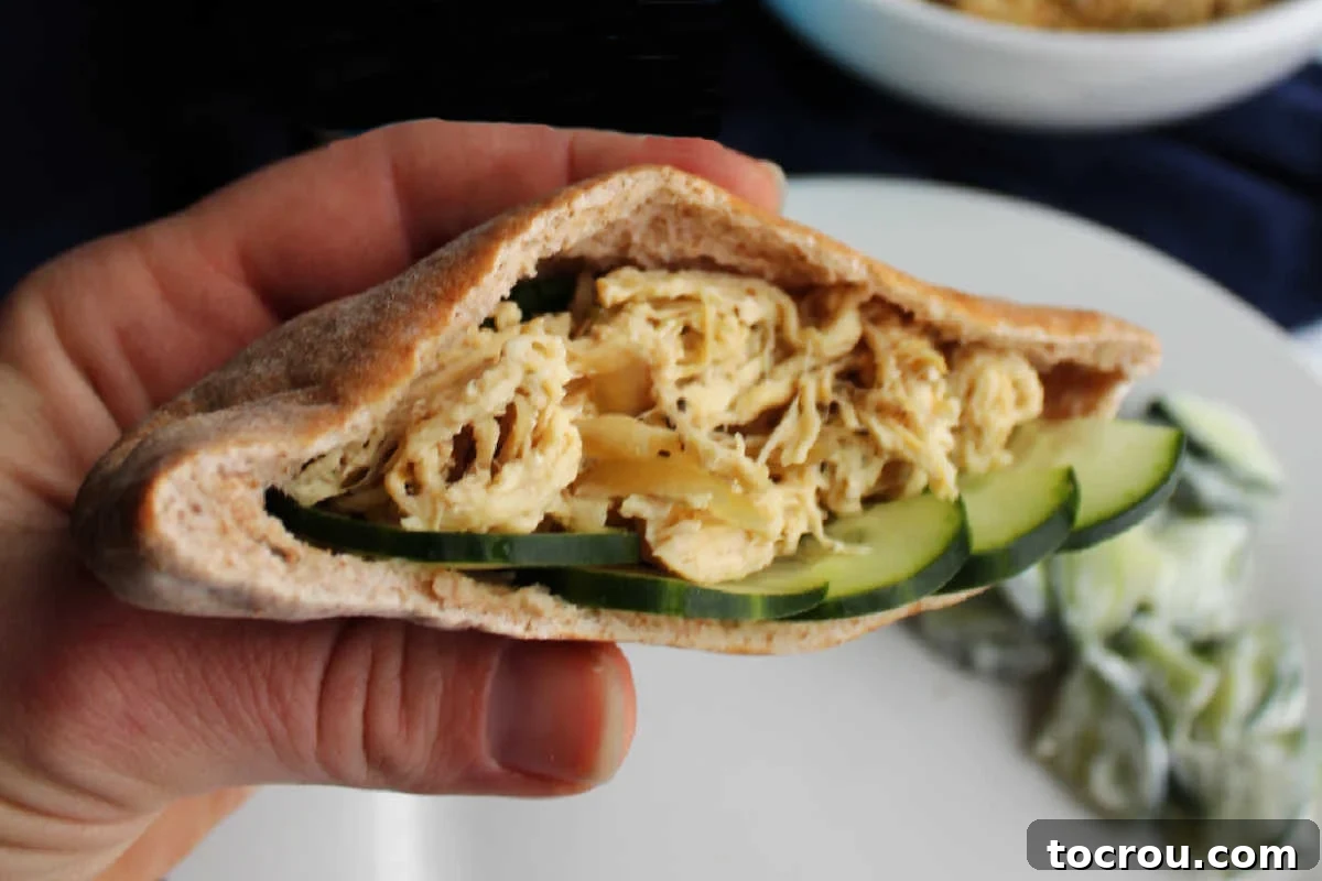 Delicious Slow Cooker Greek Chicken Pita Hand holding a pita pocket filled with shredded Greek chicken and slices of cucumber, suggesting a delicious and wholesome meal.