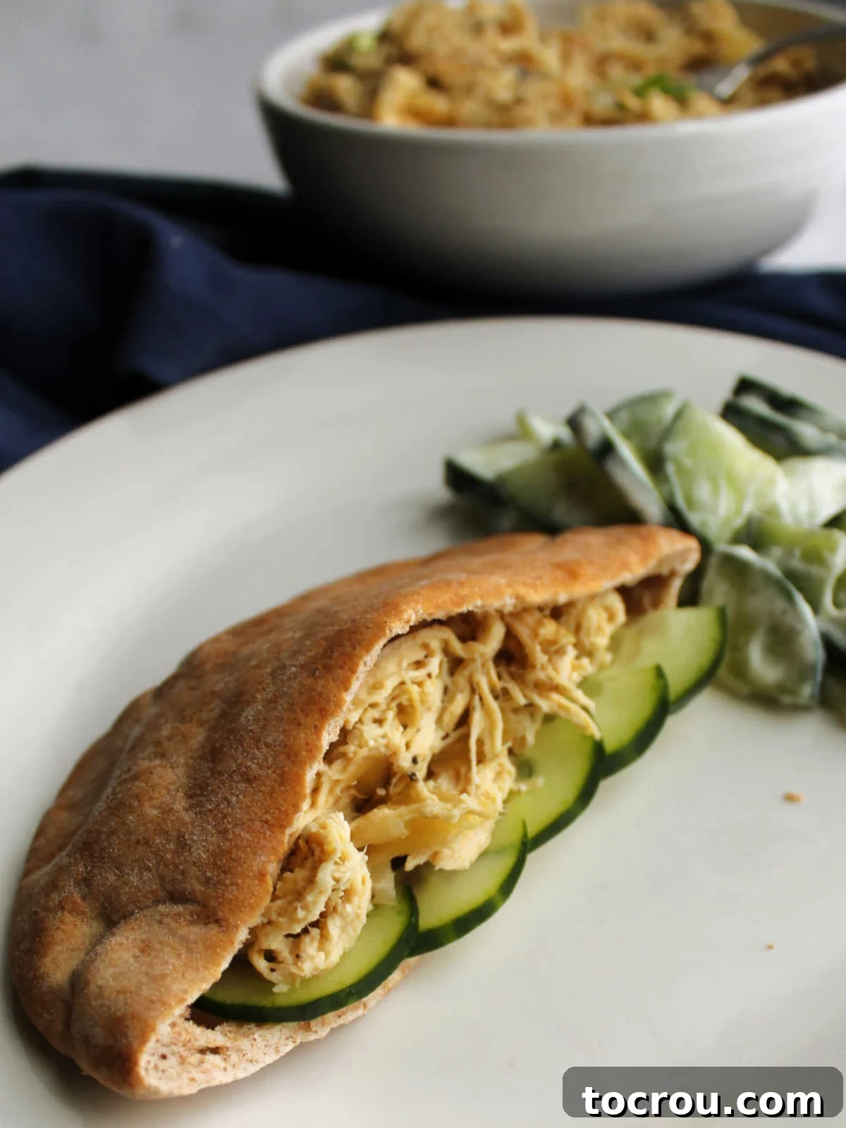 Greek Chicken Pita Sandwich with Cucumbers Dinner plate with a pita sandwich made with shredded Greek chicken and cucumber slices, ready to be enjoyed.