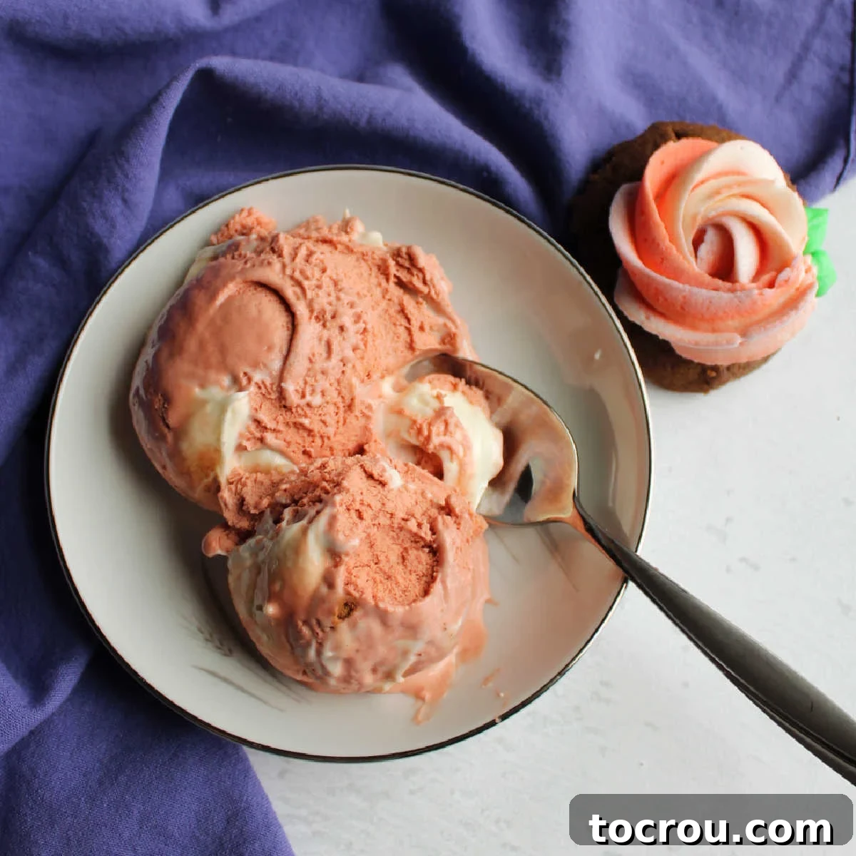 Pink Velvet Cheesecake Swirl Ice Cream 2 Bowl with two scoops of pink velvet ice cream with cream cheese swirl next to a cookie with pink and white buttercream rosette on top.