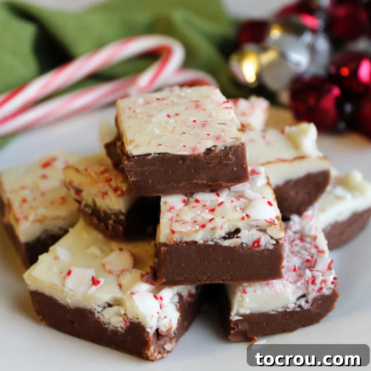 Stack of rich peppermint bark fudge with a dark chocolate bottom layer, a creamy white chocolate top layer, and a sprinkle of festive crushed candy canes.