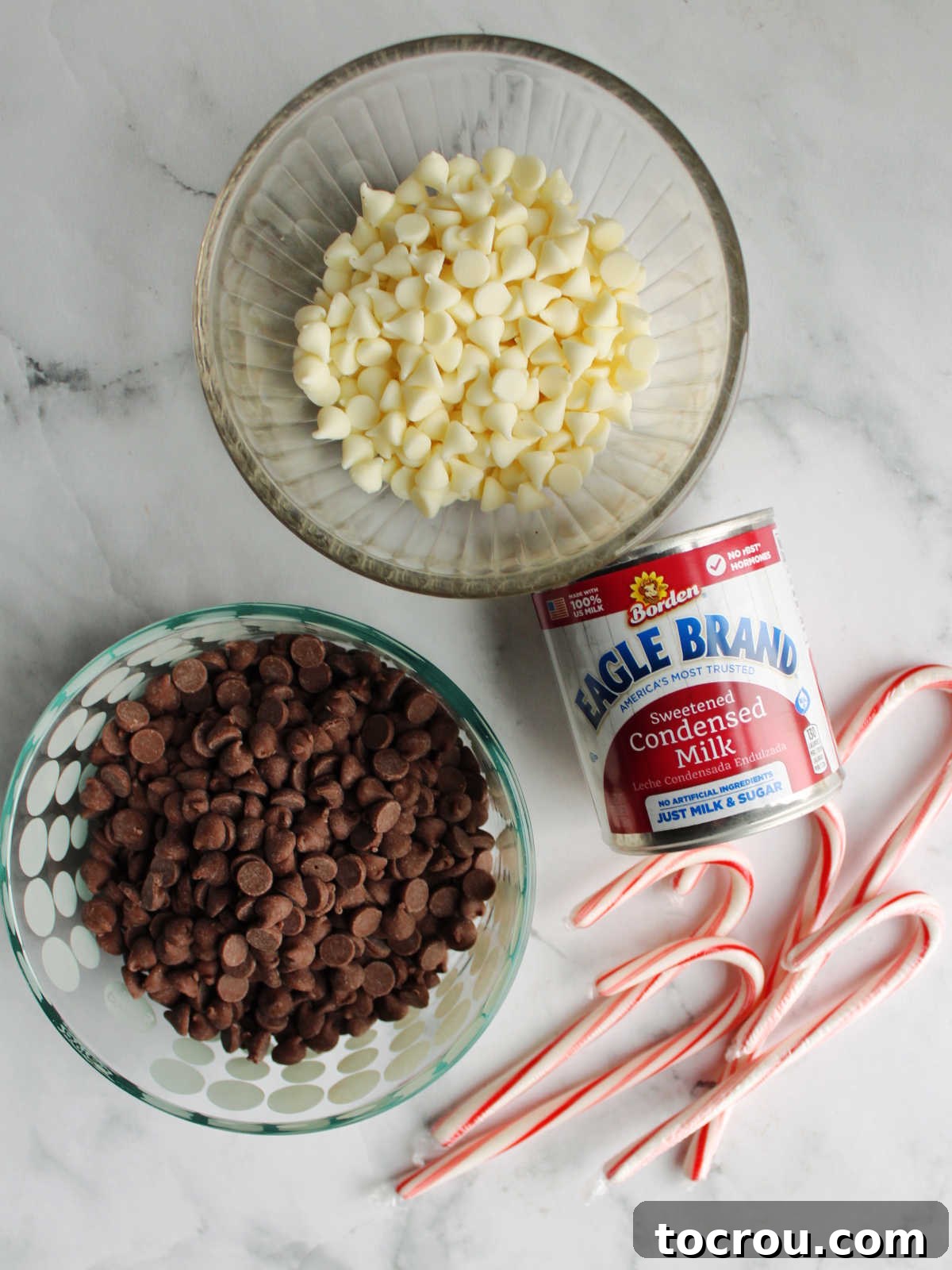 All the simple ingredients for peppermint bark fudge laid out: white chocolate chips, chocolate chips, sweetened condensed milk, and candy canes, ready for preparation.