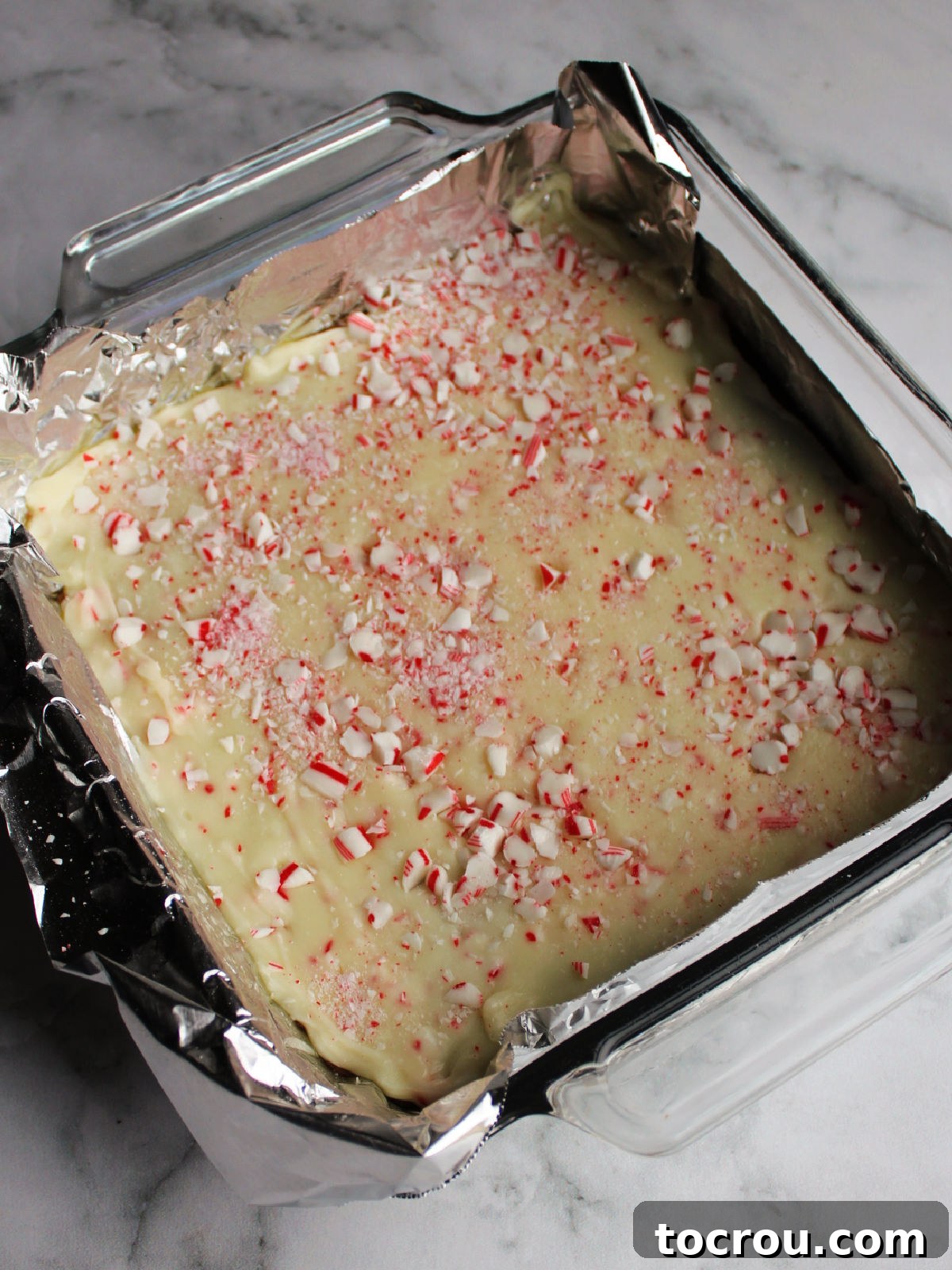 A baking pan filled with two distinct fudge layers: a chocolate base and a white chocolate top, generously adorned with pressed-in candy cane pieces.
