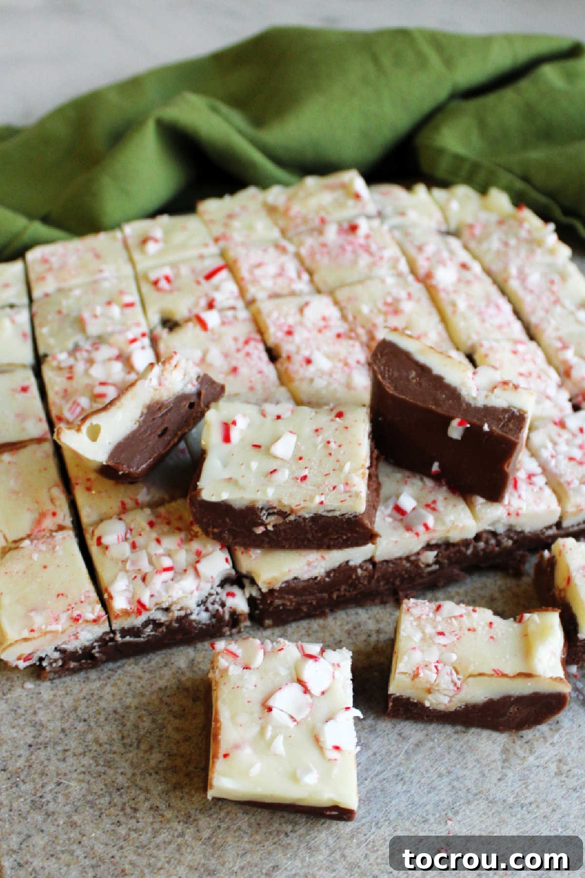 Layered candy cane fudge being expertly cut into neat squares, ready for packaging into storage containers or gifting.