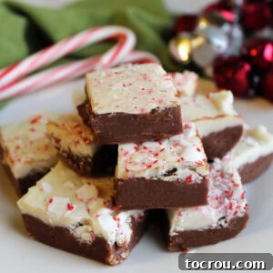 Stack of peppermint bark fudge with chocolate bottom layer, white chocolate top layer and bits of crushed candy cane on top.