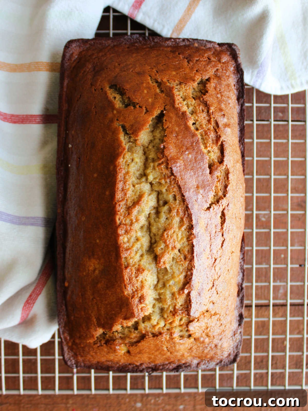 A perfectly baked loaf of banana bread, golden brown and gently cracked on top, cooling on a wire rack, ready to be sliced.