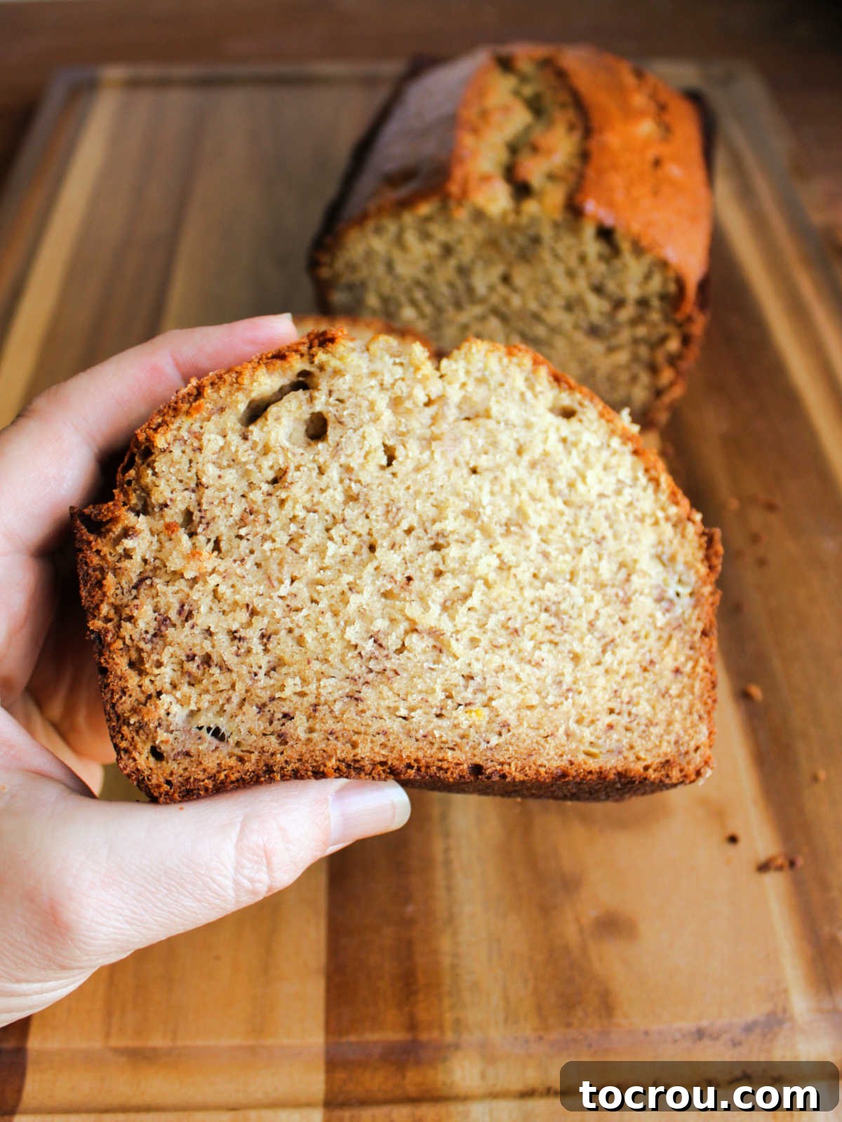 A hand holds a perfectly sliced piece of homemade banana bread, showcasing its inviting texture and readiness to be savored.