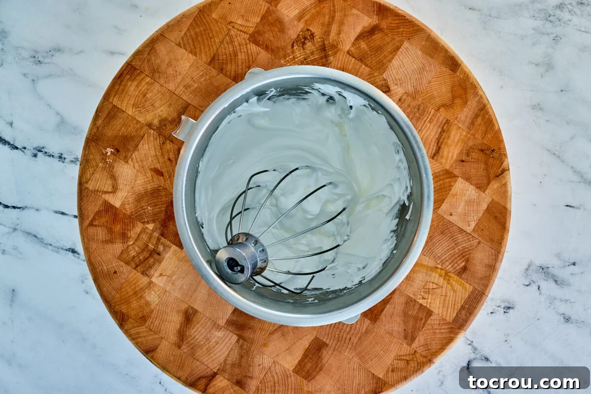 A mixer bowl and whisk, proudly displaying a voluminous, fluffy white meringue, perfectly prepared and ready to grace the pie.