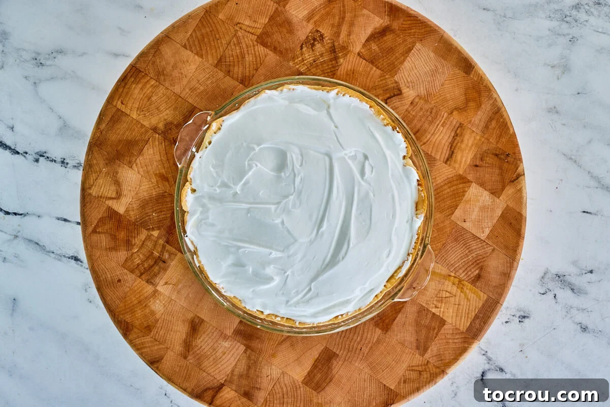 A layer of pristine meringue, expertly spread over the warm pie filling, creating a seamless seal from edge to edge, poised for baking to achieve its golden perfection.