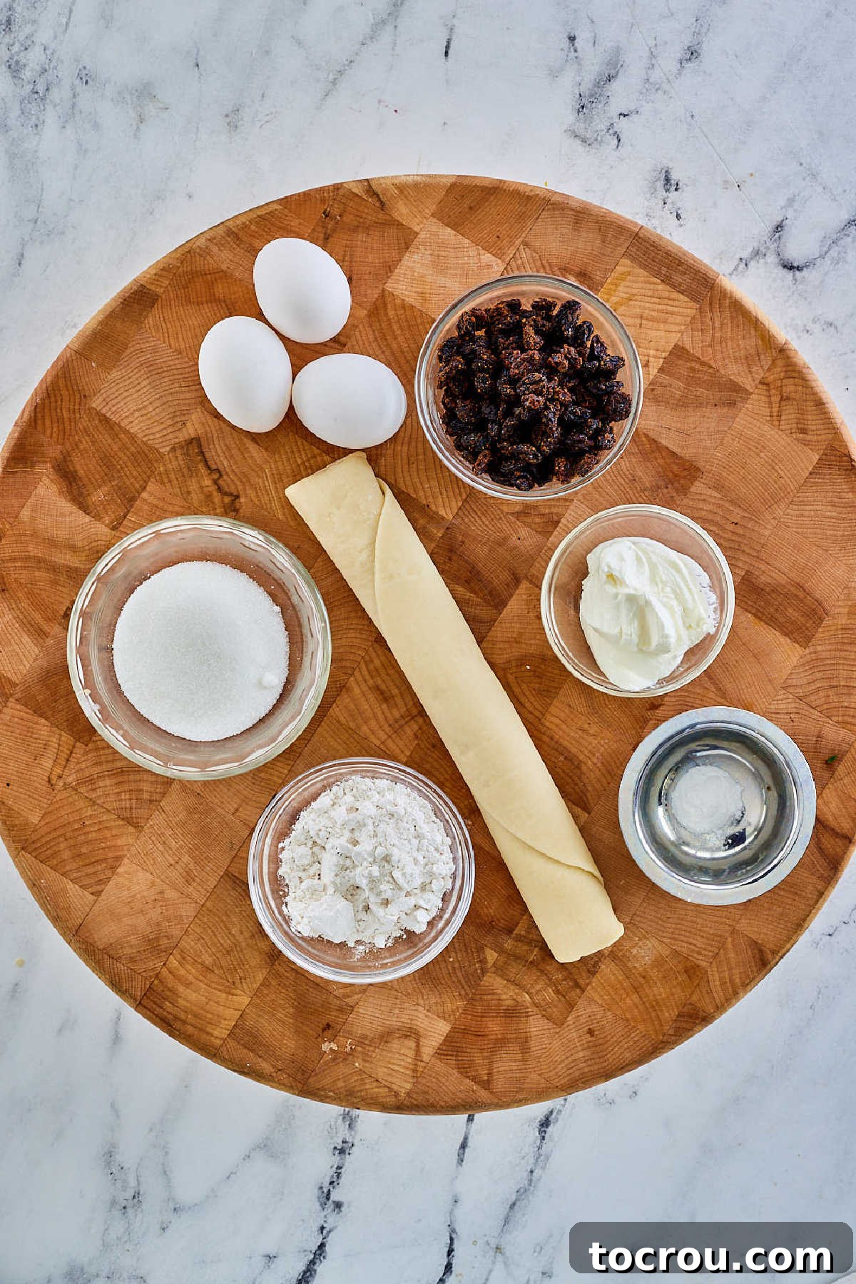 A flat lay photograph of all the essential ingredients laid out: a prepared pie pastry, fresh eggs, creamy sour cream, granulated sugar, all-purpose flour, cream of tartar, and succulent raisins, poised for pie creation.