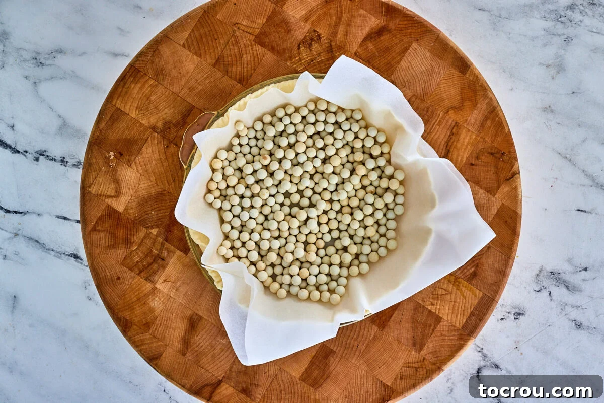 An unbaked pie crust, perfectly fitted into a pie pan and filled with parchment paper and pie weights, ready for blind baking.