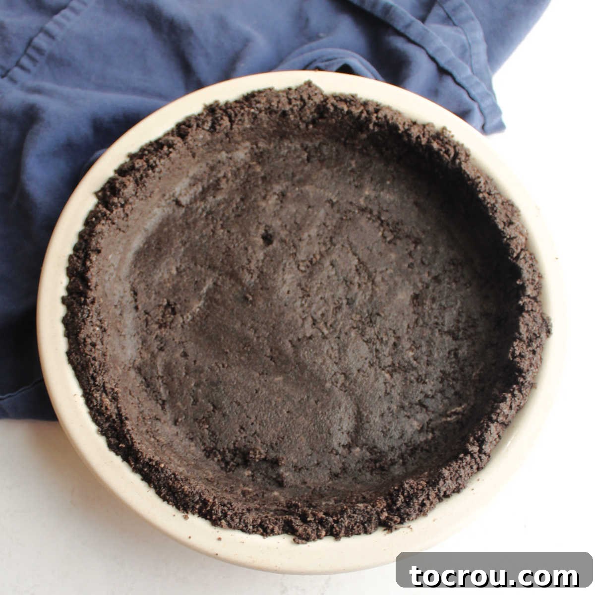 A perfectly formed no-bake Oreo pie crust in a glass pie plate, ready for delicious filling. The crust is dark chocolate, showcasing its rich Oreo origins.