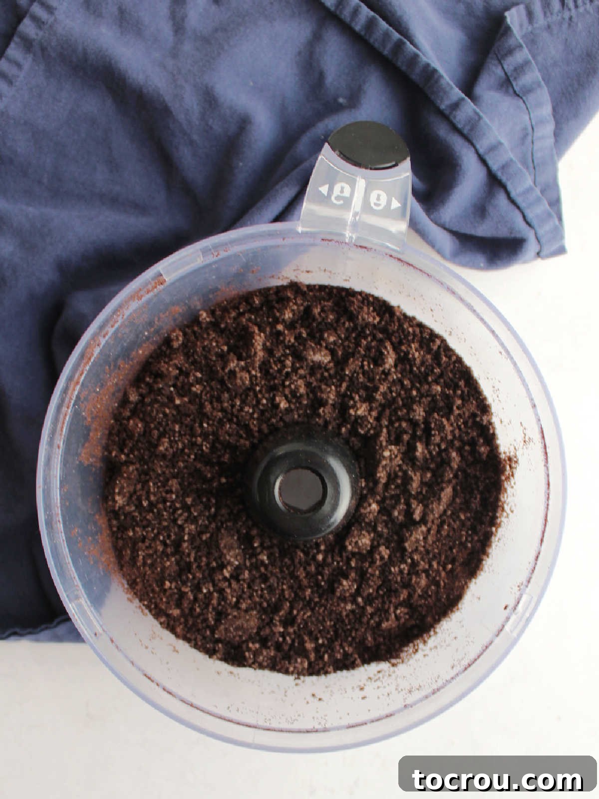 Finely crushed Oreo crumbs inside a food processor, perfectly prepared for mixing with butter to form the pie crust.