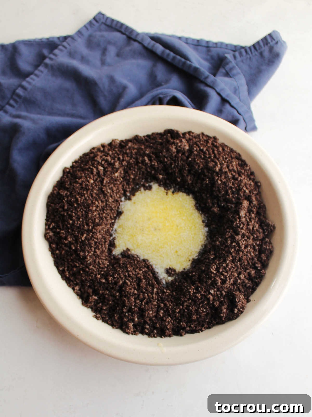 Oreo crumbs neatly arranged in a pie plate with a pool of melted butter in the center, awaiting thorough mixing to create the crust.