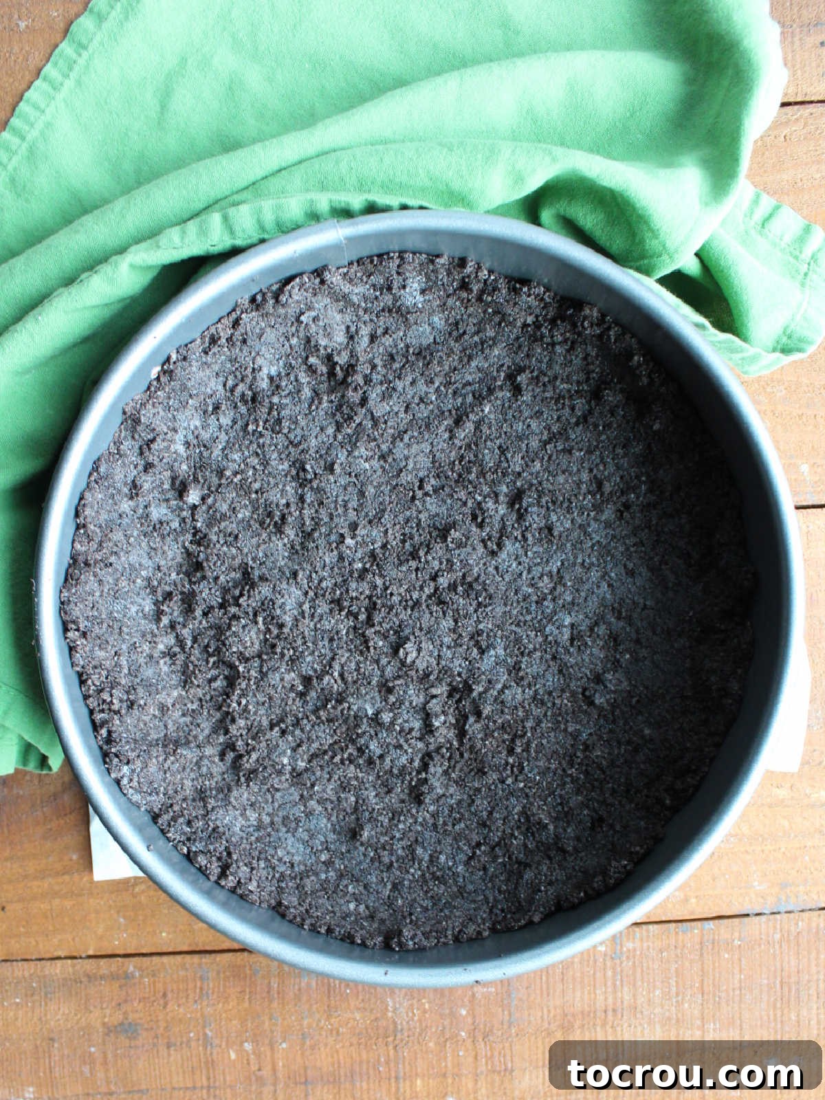 Oreo crumbs and melted butter pressed into a firm, even crust at the bottom of a springform pan, ready for chilling.