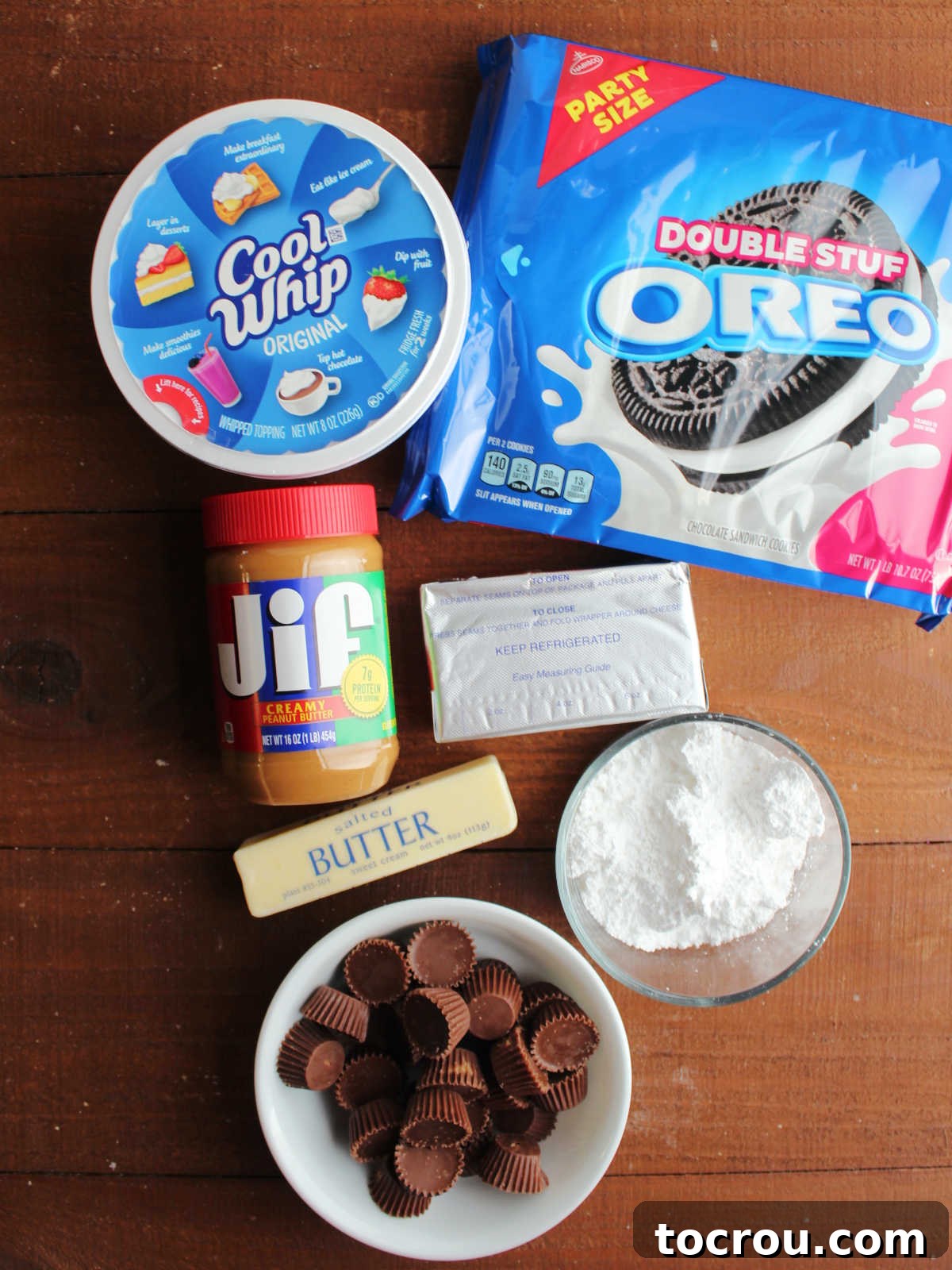 Ingredients for no bake peanut butter pie laid out, including peanut butter, cream cheese, powdered sugar, cool whip, oreos, butter, and Reese's peanut butter cups.