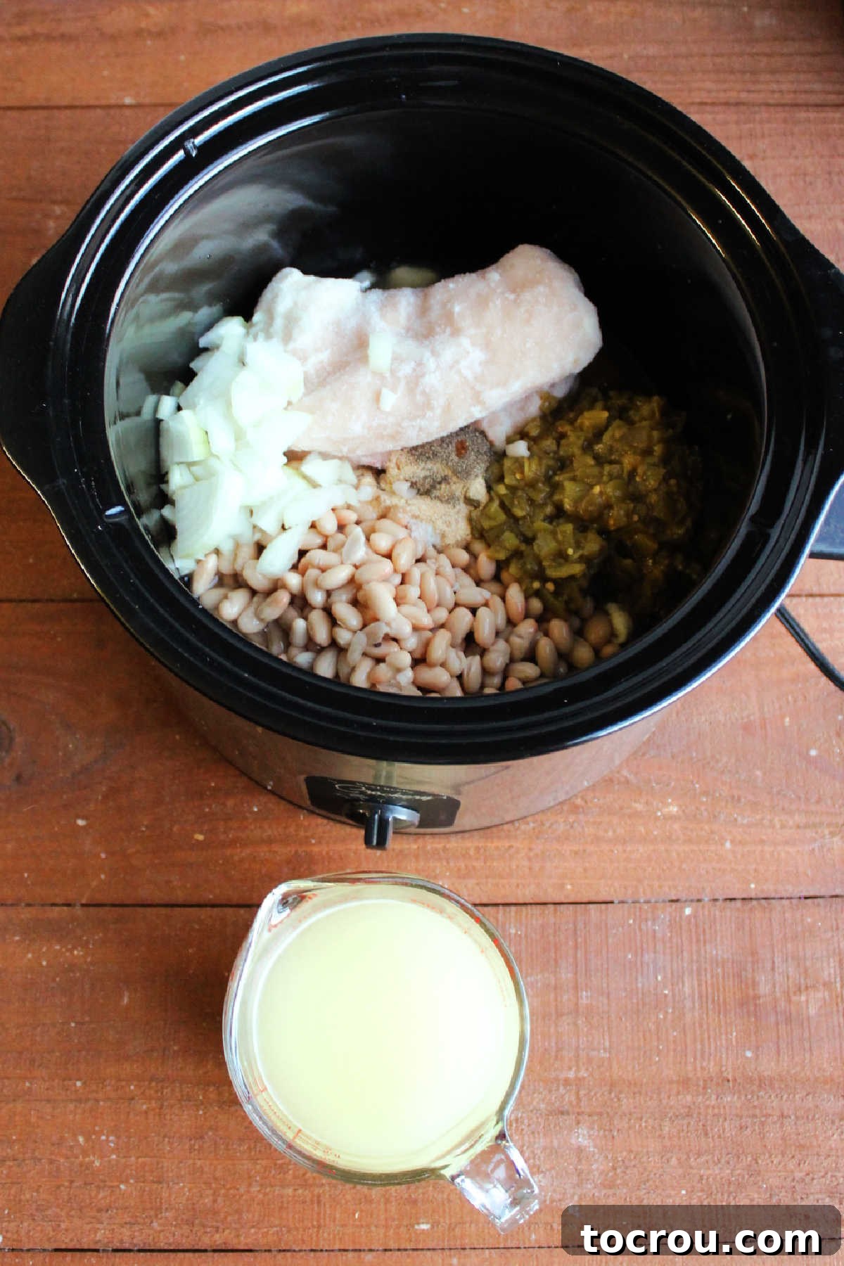 Prepping Chili in Slow Cooker All ingredients except sour cream and half-and-half placed in a slow cooker, with a measuring cup of chicken broth being poured in.