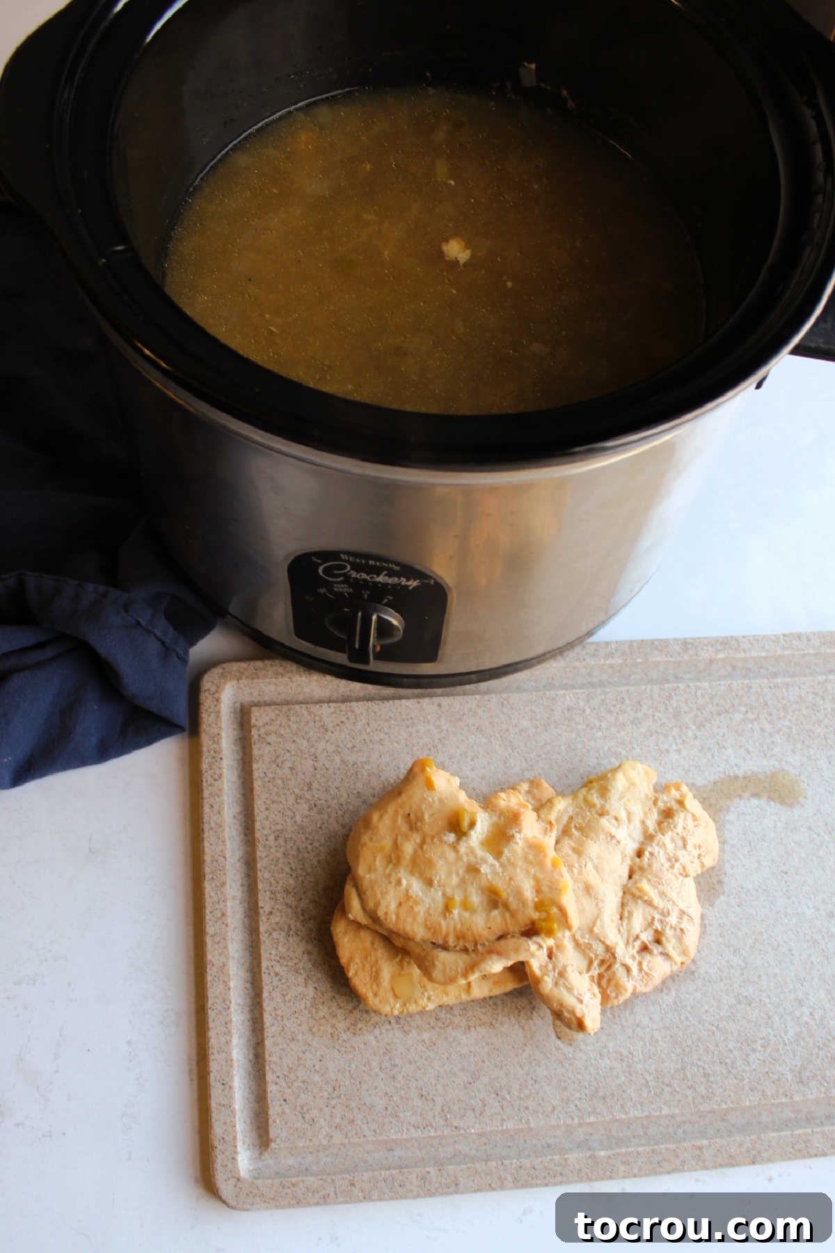 Chopping Cooked Chicken for Chili Cooked chicken breast removed from the slow cooker and resting on a cutting board, ready to be chopped into bite-sized pieces and returned to the chili.