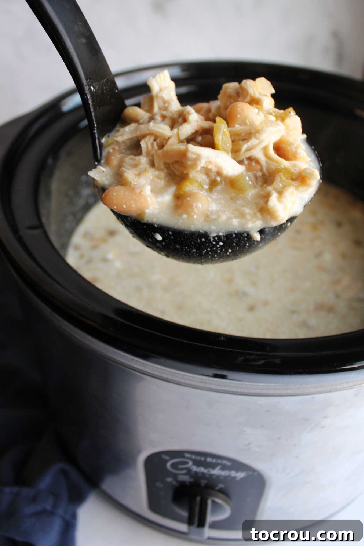 Serving Slow Cooker White Chicken Chili A ladle scooping out a generous portion of creamy white chicken chili directly from the crockpot, showing its rich texture.