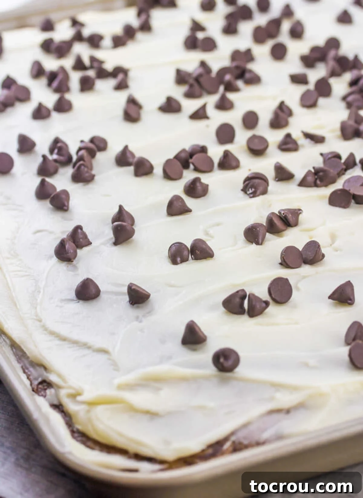 The Ultimate Chocolate Chip Cookie Dough Texas Sheet Cake 3 Looking down on sheet pan filled with chocolate chip cookie dough cake topped with smooth white icing and lots of chocolate chips.