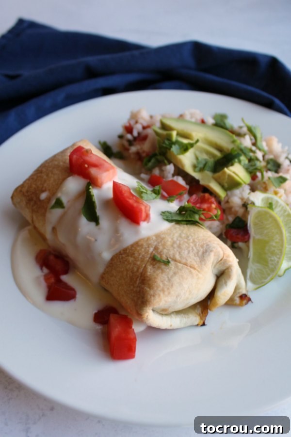 Crispy Baked Barbacoa Chimichangas 6 A beautifully plated baked chimichanga with white queso, chopped tomatoes, and fresh cilantro, served alongside Mexican rice, lime wedges, and avocado slices.
