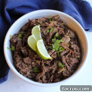 Bowl of barbacoa style venison with wedges of lime, ready to be put in a tortilla.