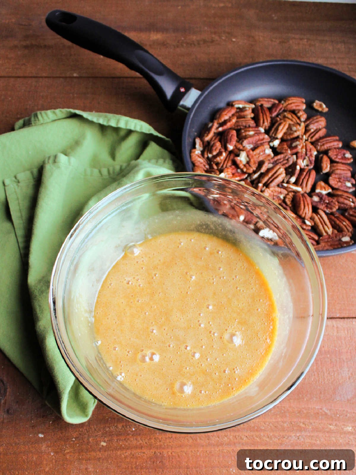 Golden Caramel Pecan Delight 6 Bowl of pie filling mixture with caramel and eggs all mixed together with toasted pecans in a skillet nearby.