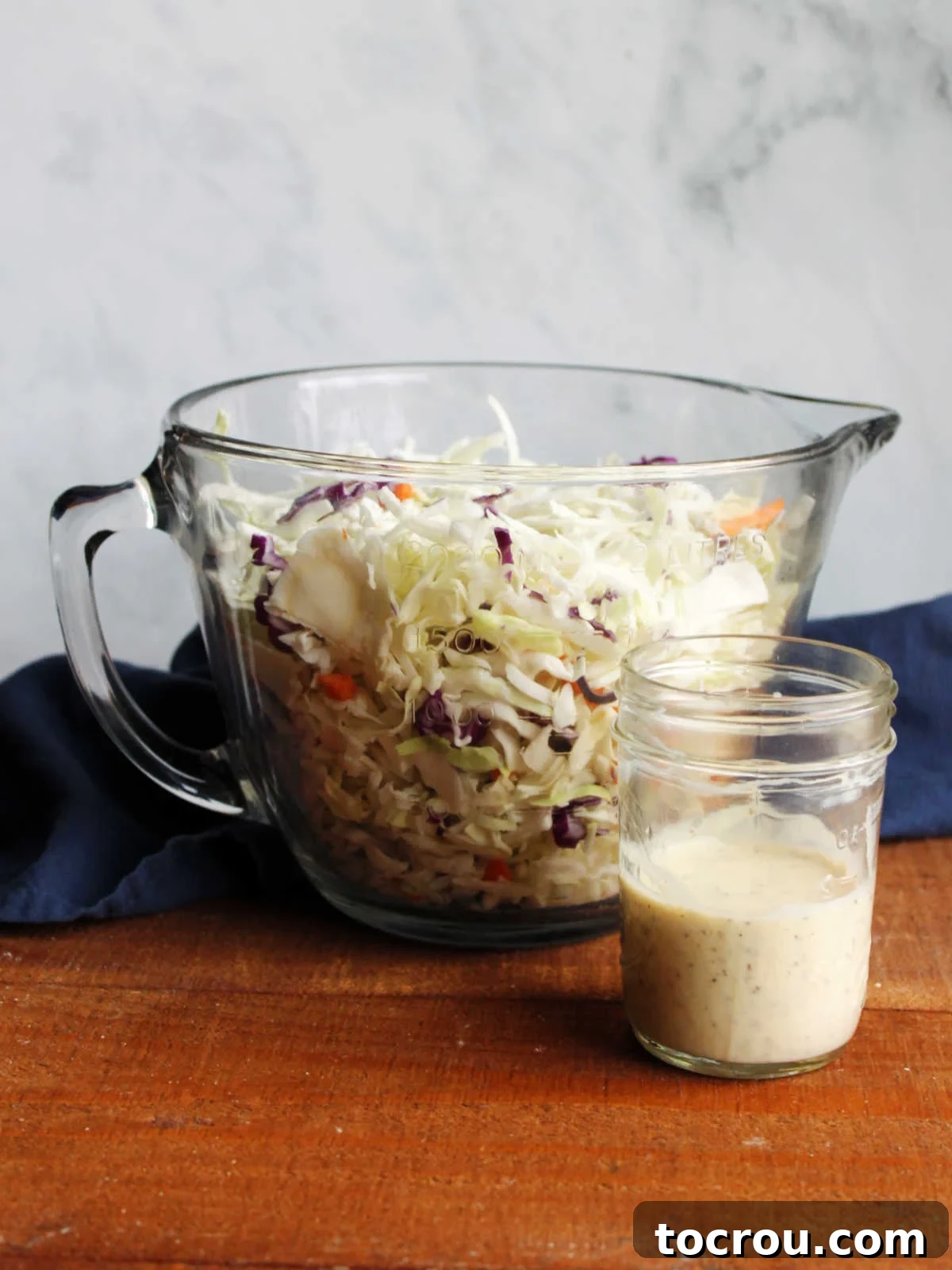 Cabbage and Dressing Large glass bowl filled with shredded cabbage next to a jar of creamy condensed milk dressing.