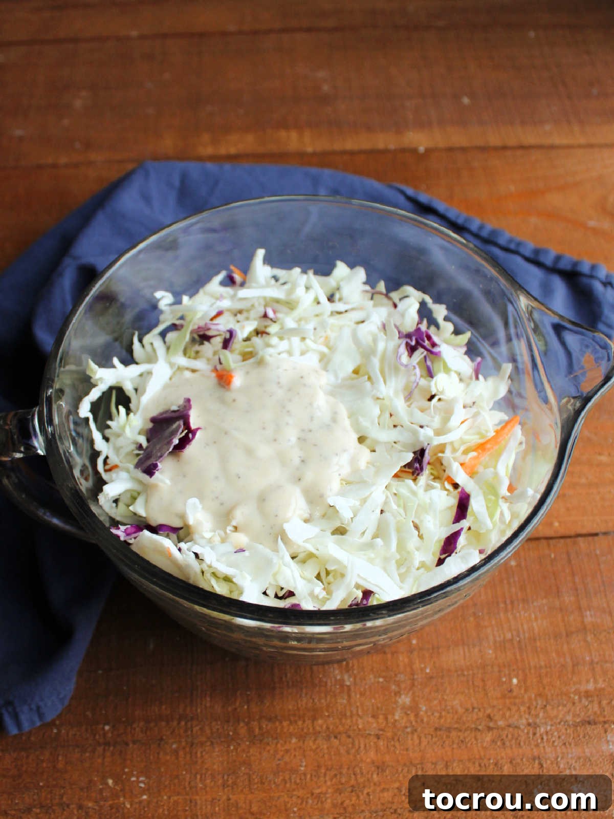 Dressing Starting to Coat Small pool of creamy dressing on top of shredded cabbage in a glass bowl, just beginning to meld.