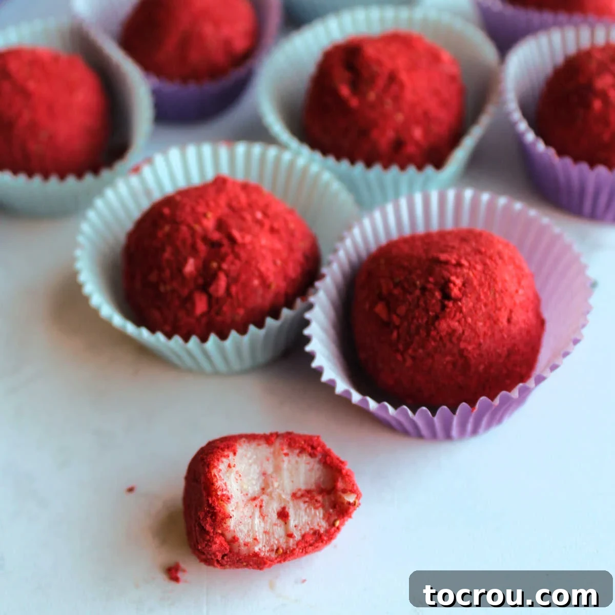Strawberry brigadeiro with a bite missing showing creamy pink interior and red freeze-dried strawberry powder on the outside.