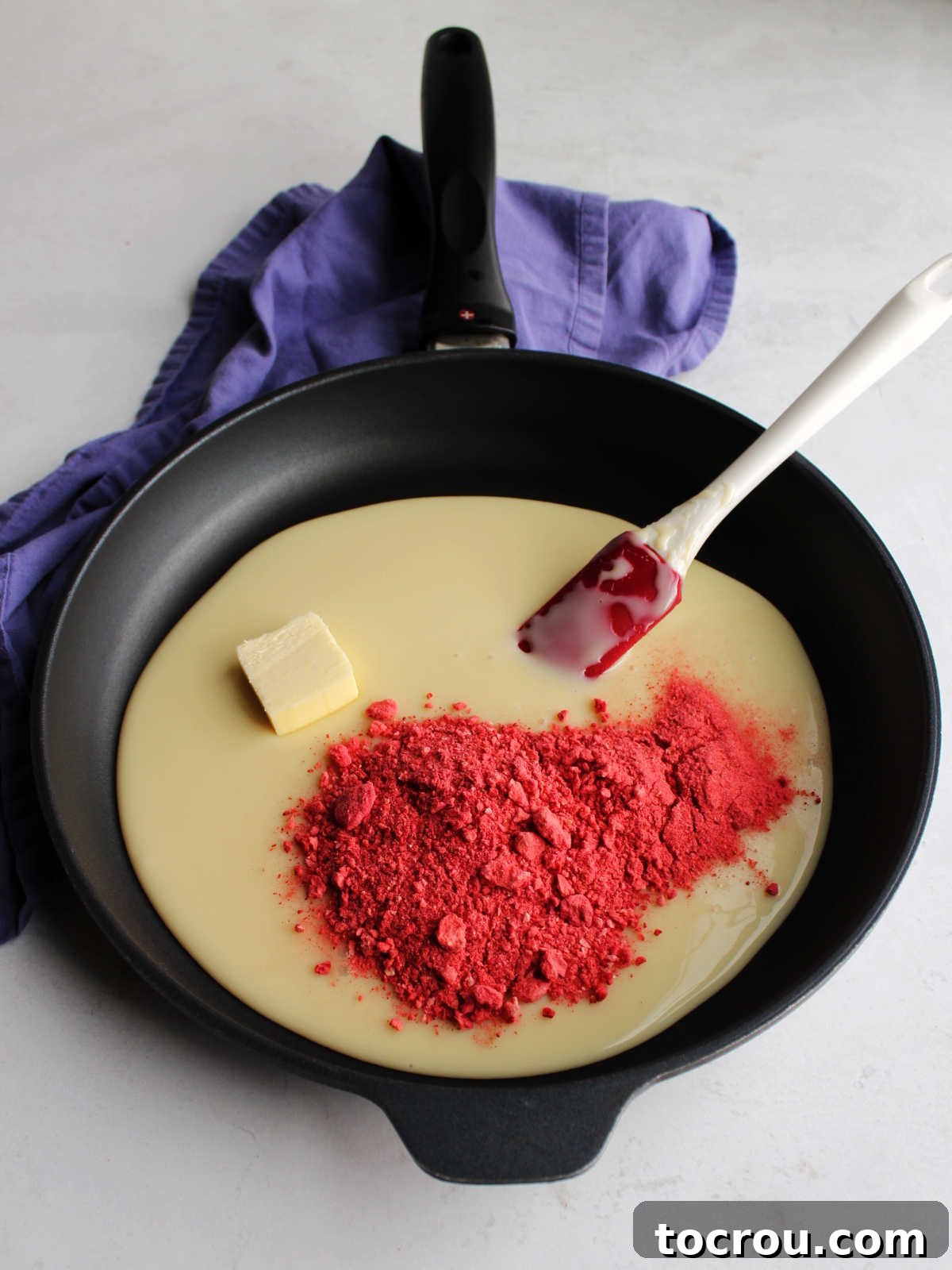 Skillet with condensed milk, butter and crushed freeze-dried strawberries inside ready to cook.