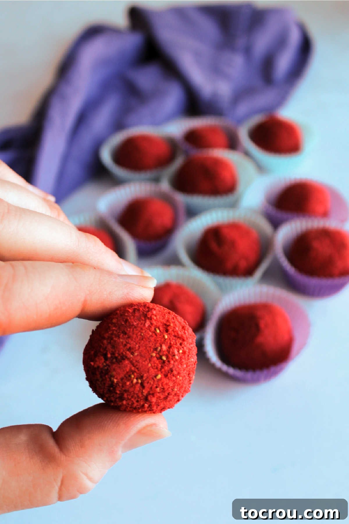 Hand holding red strawberry truffle candy with more balls of candy in the background.