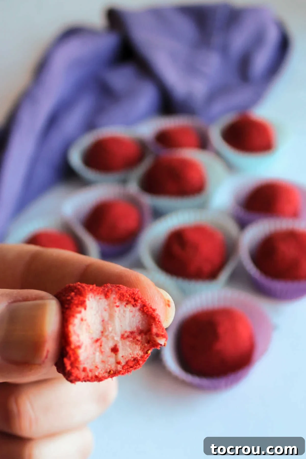 Hand holding strawberry brigadeiro truffle with bite missing showing soft pink inside. 