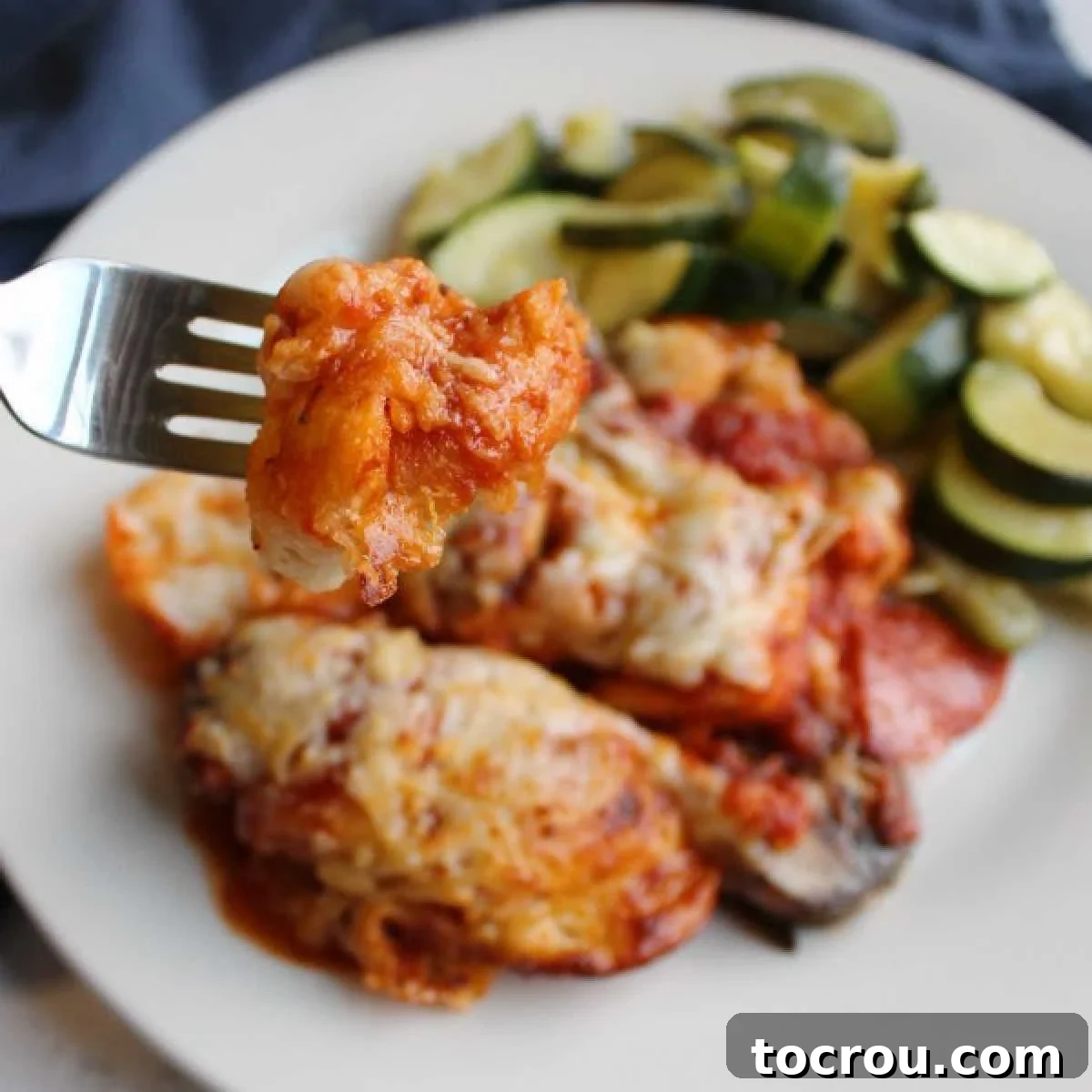 A delectable bite of pepperoni bubble up pizza on a fork, with a blurred dinner plate in the background.