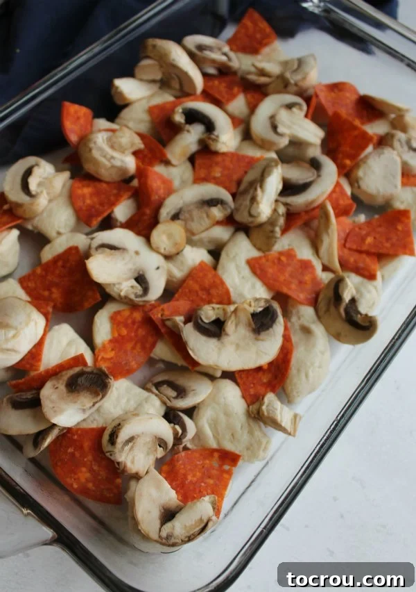 Unbaked biscuits with pepperoni and mushrooms carefully arranged in a baking pan, ready to transform into a delicious pizza casserole.