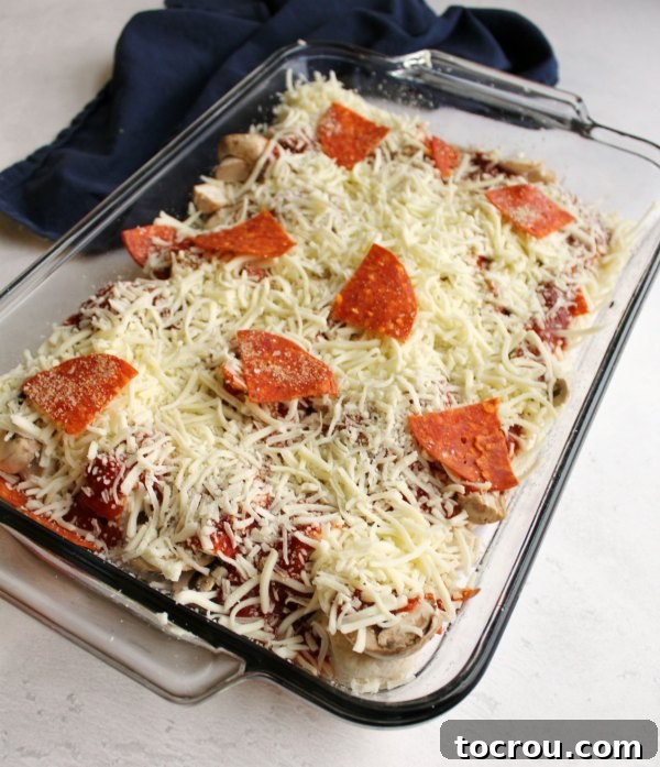 A baking pan filled with bubble up pizza, generously covered with shredded mozzarella cheese and pepperoni slices, poised for the oven.