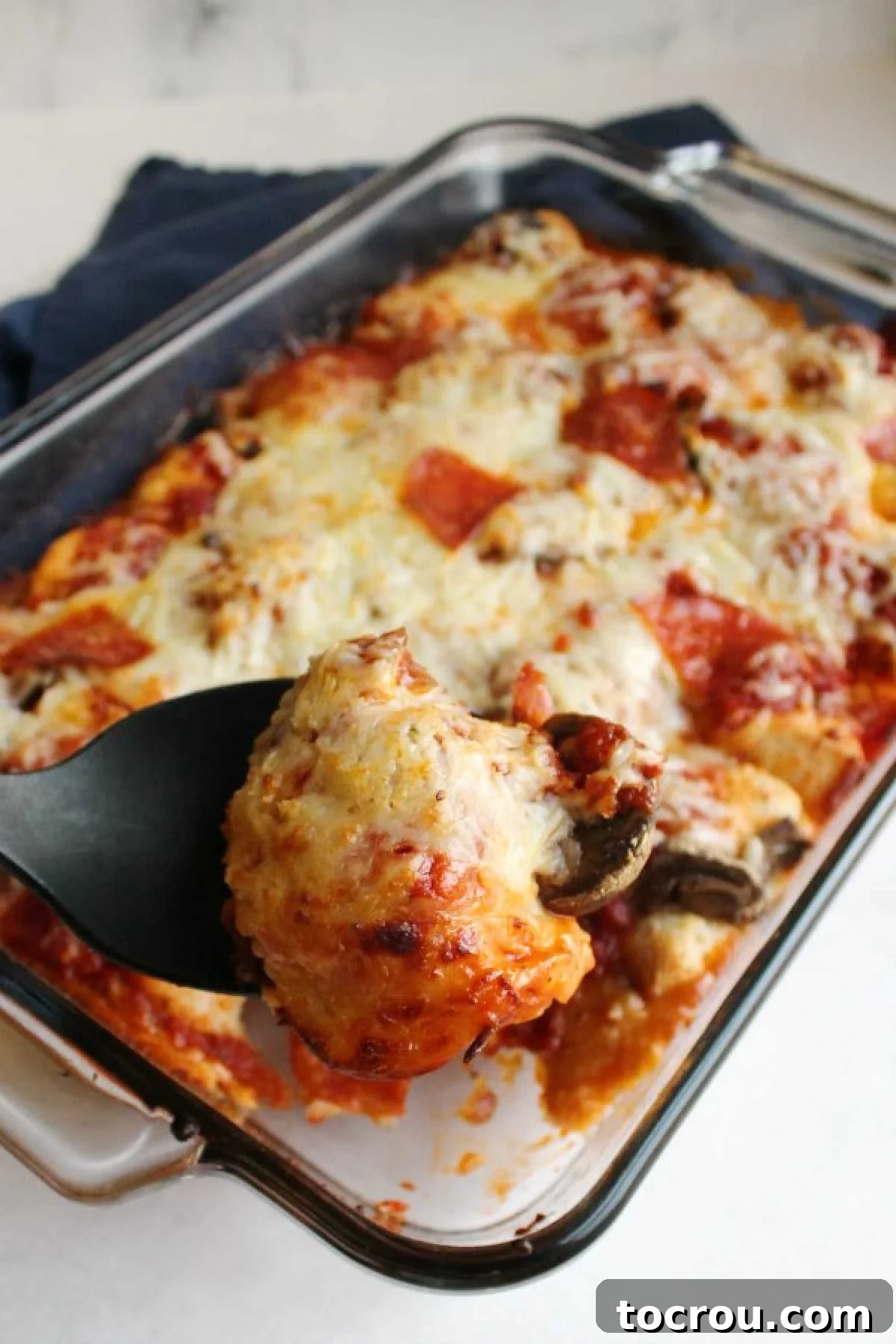 A serving spoon lifting a generous portion of bubble up pizza, revealing gooey melted cheese, rich sauce, and tender biscuit bites.