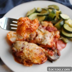 A delectable bite of pepperoni bubble up pizza on a fork, with a blurred dinner plate in the background.