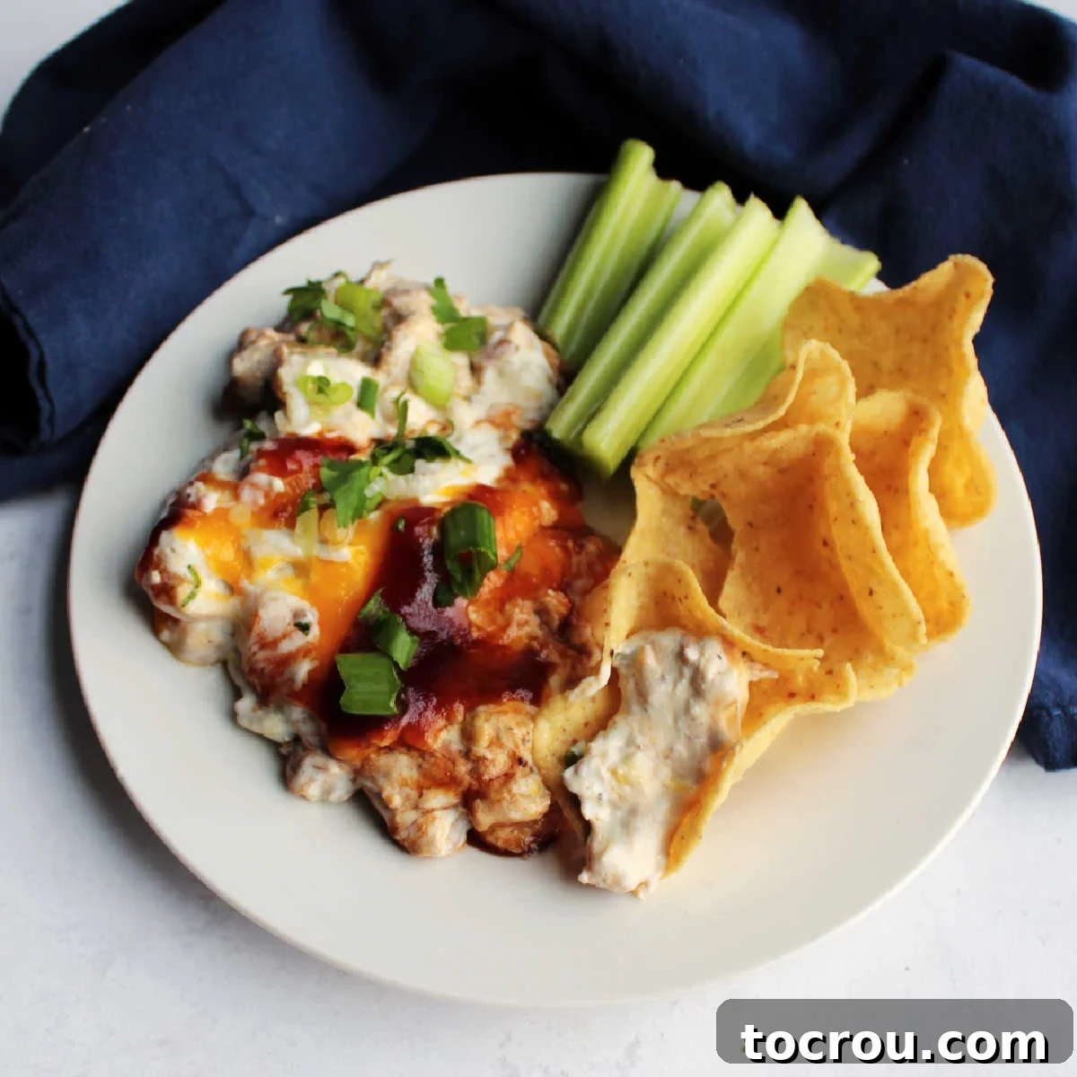 Warm cheesy dip filled with pulled pork and corn is hearty and delicious. It's a great snack for a bbq or game day. A small plate showcasing creamy pulled pork dip, surrounded by crispy tortilla chips and refreshing celery sticks, ready for dipping.